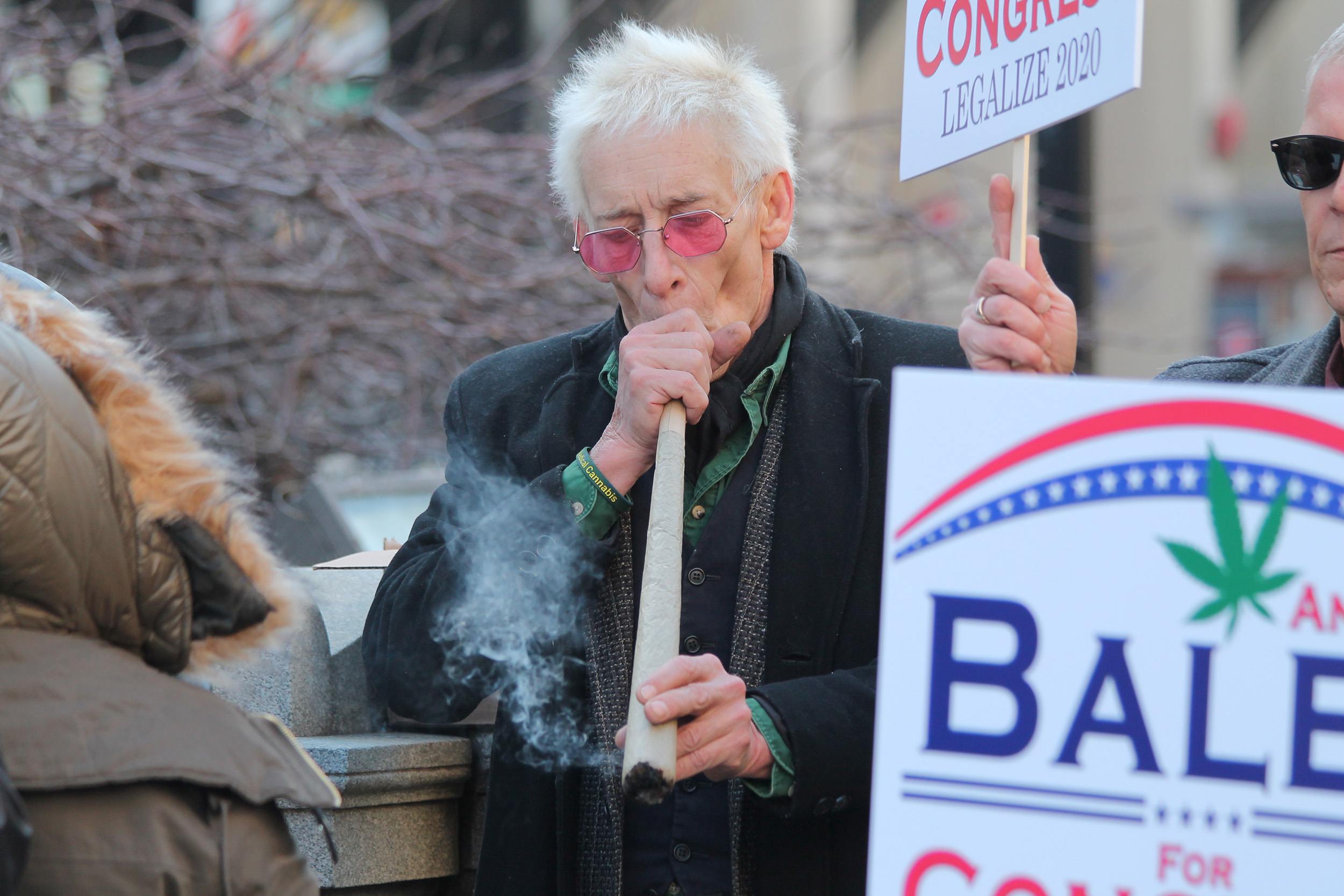 Bill Levin smokes a three-foot long blunt. He has white hair and wears glasses with pink lenses.